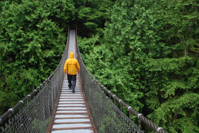 Person in a rain jacket walking across Lynn Canyon suspension bridge in North Vancouver, BC