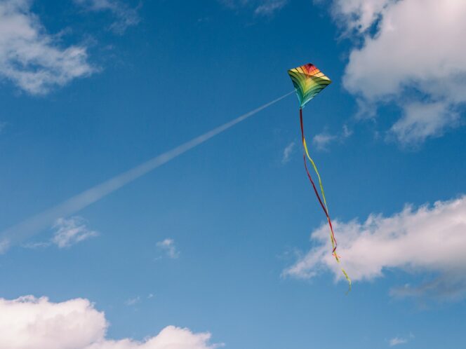 A kite flies against a blue sky with wispy clouds