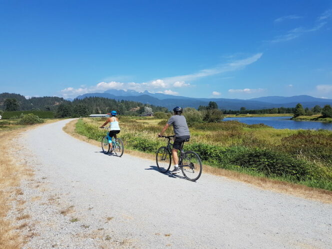 Two cyclists ride along a dyke trail in Pitt Meadows on a tour with Into the Wild Cycing Tours