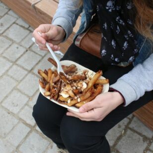 A person holds a take-out container of poutine on their lap