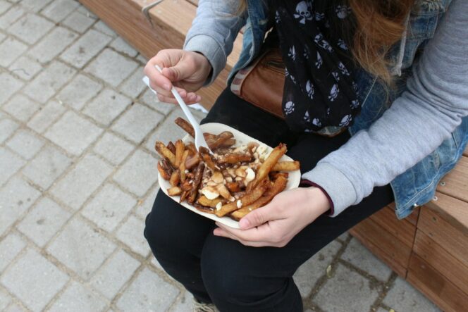 A person holds a take-out container of poutine on their lap