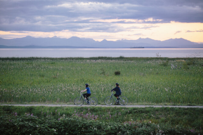 Two people cycle the West Dyke Trail in Richmond at sunset