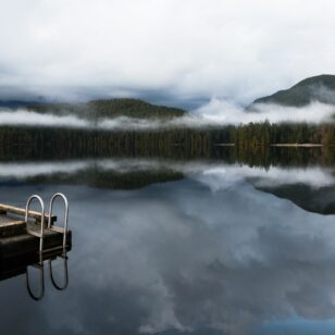 A man in a yellow coat stands on a floating dock at Sasamat Lake near Vancouver