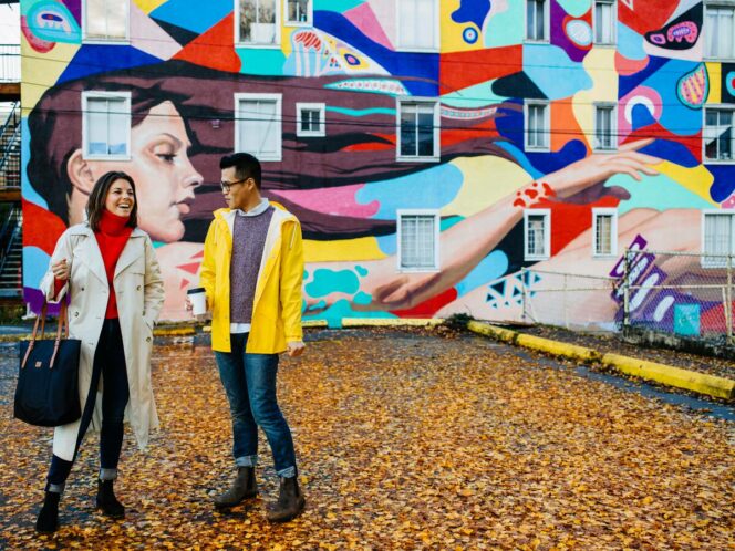 Two people standing in front of a colourful mural in Mount Pleasant as part of the Vancouver Mural Festival.