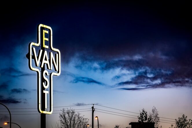 An illuminated cross with the words East Van against the night sky. 