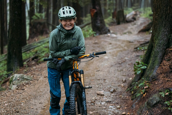 Betty Birrell smiles and leans against her mountain bike on a wet trail in North Vancouver