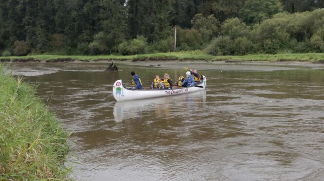 A group of adults and children paddles a canoe in Kanaka Creek