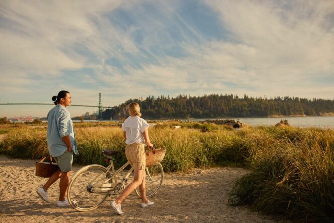 A couple with a bike in Ambleside Park with a view of the Lions Gate Bridge.