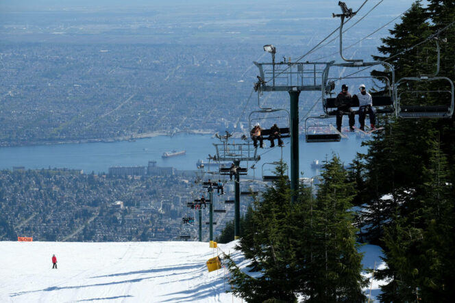Skiers ride the chairlift at Grouse Mountain with the city in the background.