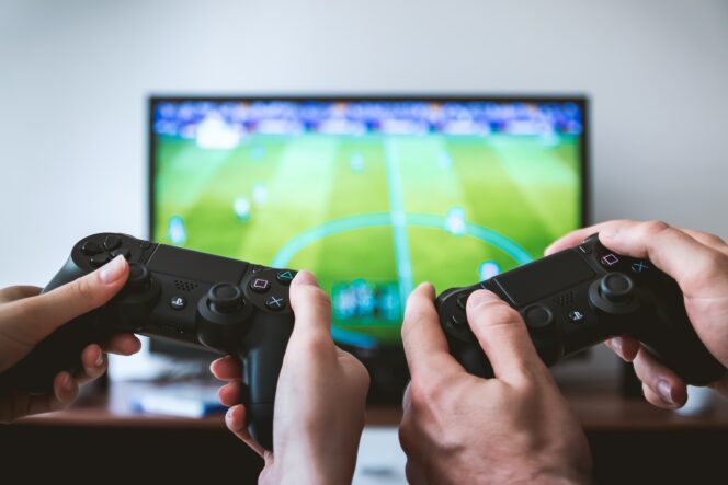 Two people hold game controllers in front of a soccer video game