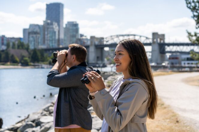 A man and a woman hold binoculars and look for birds in Vanier Park in Vancouver
