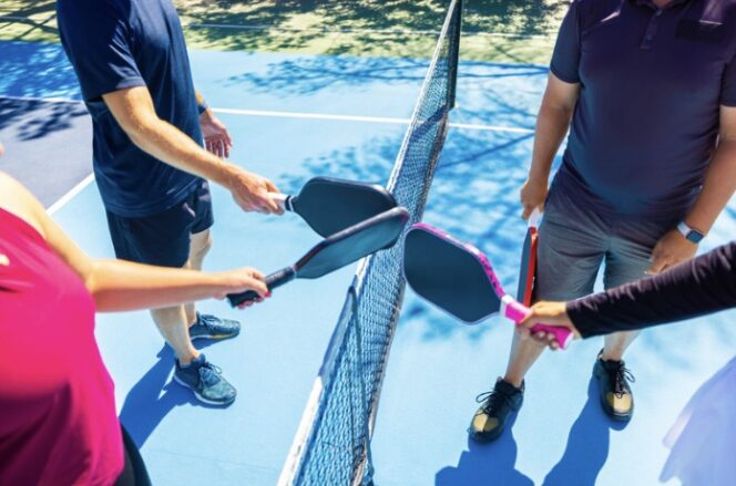 Pickleball players touch paddles at the top of a net